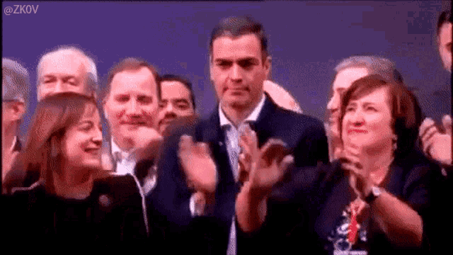 a man in a suit stands in front of a crowd of people applauding