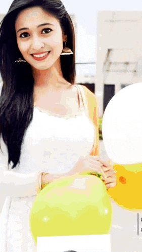 a woman in a white dress is holding a yellow balloon and smiling