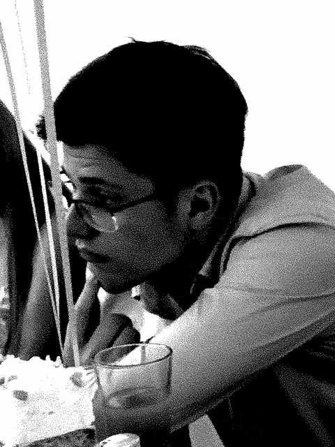 a man wearing glasses sits at a table with a glass in his hand