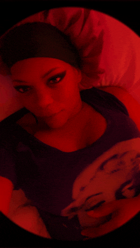 a woman in a purple shirt is laying on a bed with a red background