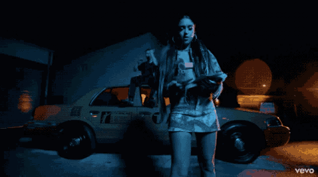 a woman stands in front of a yellow car with the word vevo on the bottom right