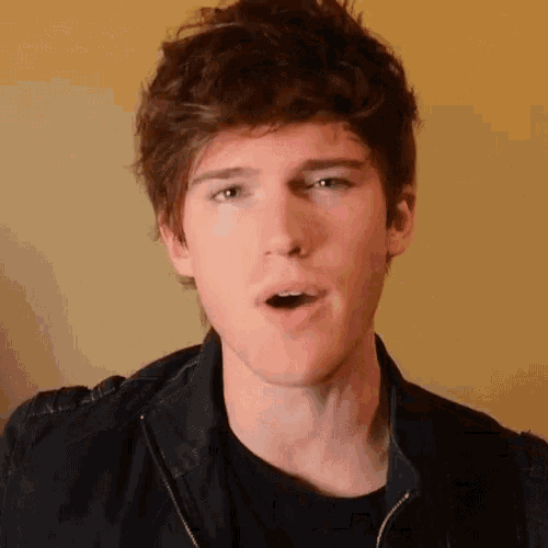 a young man wearing a black jacket and a black shirt is making a surprised face