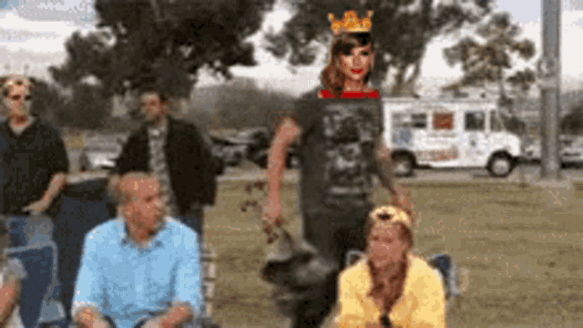 a group of people sitting in a park with a woman wearing a crown in the background