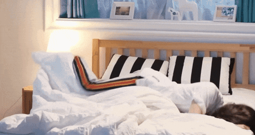 a bed with white sheets and black and white striped pillows has a picture of a horse on the window sill