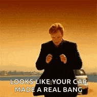 a man in a suit is standing in front of a car and looking like his car made a real bang .