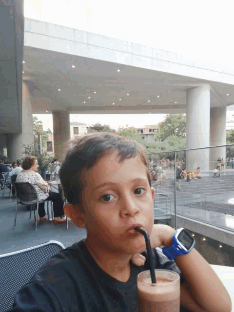 a young boy drinking a smoothie with a straw and a watch on his wrist