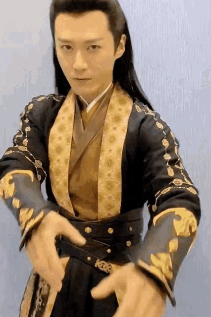 a man with long hair is wearing a black and gold costume with gold trim .