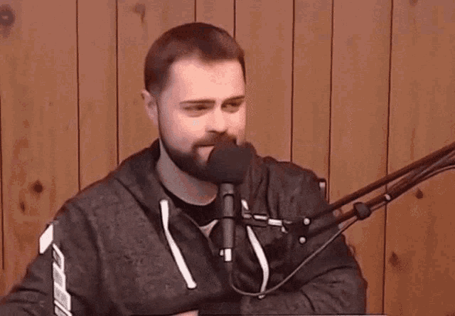 a man with a beard is standing in front of a microphone and laughing .