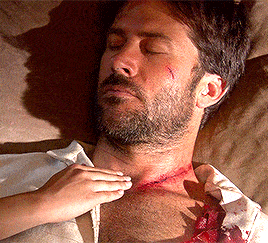 a man with a scar on his neck is laying on a bed with his eyes closed