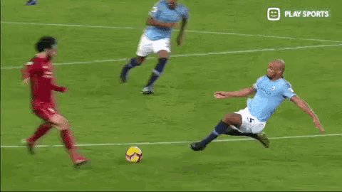 a soccer player in a red jersey is kicking another player in a blue shorts on a field .
