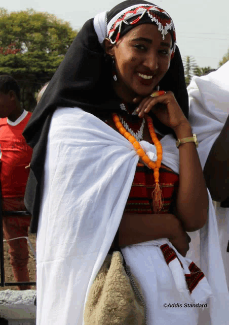 a woman wearing a black head scarf and a white dress is smiling with addis standard written in the corner