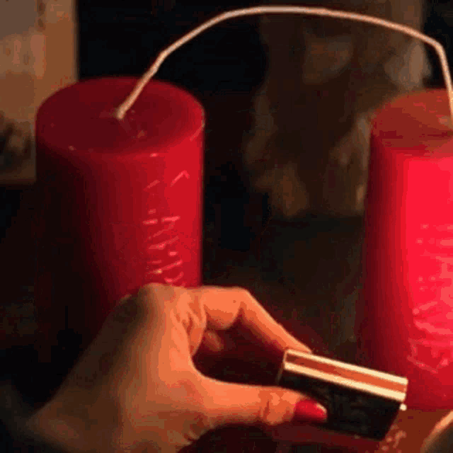 a woman 's hand is holding a match in front of two red candles .