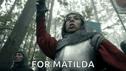 a man in a knight 's armor is holding a sword in a forest and shouting .