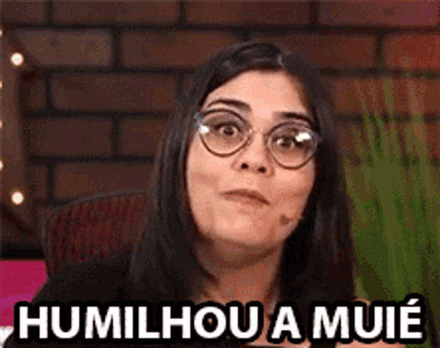 a woman wearing glasses is sitting in front of a brick wall and says humilhou a muie