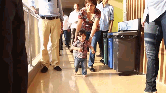 a woman holds a child 's hand while walking down a hallway with recycling bins