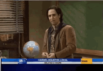 a man stands in front of a globe with the words hardin-houston local on the screen