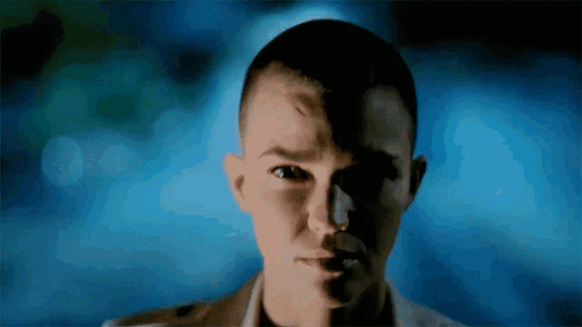 a close up of a woman 's face with a shaved head and a blue background