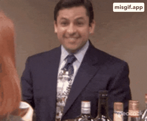 a man in a suit and tie is smiling while standing in front of a bottle of alcohol .