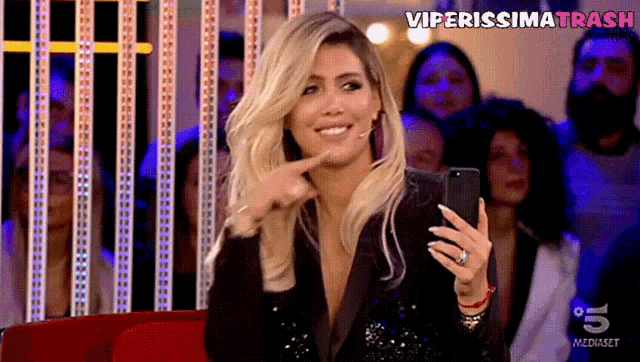 a woman sitting in front of a crowd holding a cell phone and pointing at it with the words viperissima trash above her