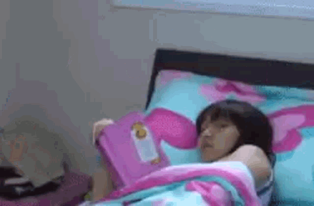 a little girl is laying in bed reading a pink book