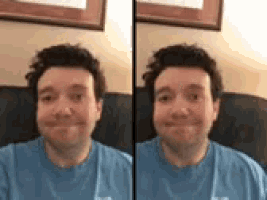 a man in a blue shirt is sitting on a couch and making a funny face .