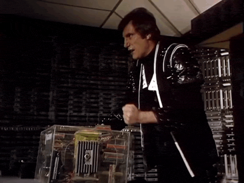 a man in a black and white suit is standing in front of a machine and says damn it