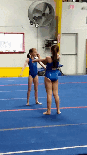 two girls in blue leotards are standing on a blue floor