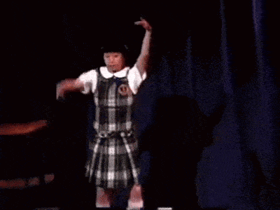 a woman in a school uniform is dancing on a stage .