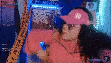 a woman wearing a pink hat and headphones stands in front of a warning tape that says " happy halloween "