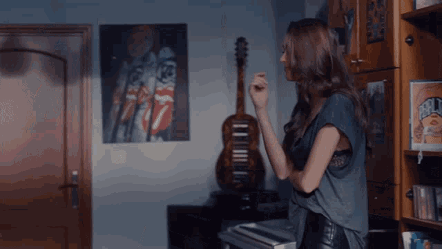 a woman stands in front of a guitar and a rolling stones poster on the wall