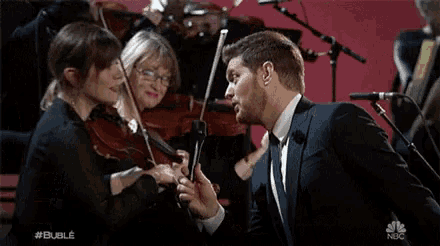 a man in a suit and tie is singing into a microphone in front of a violin orchestra