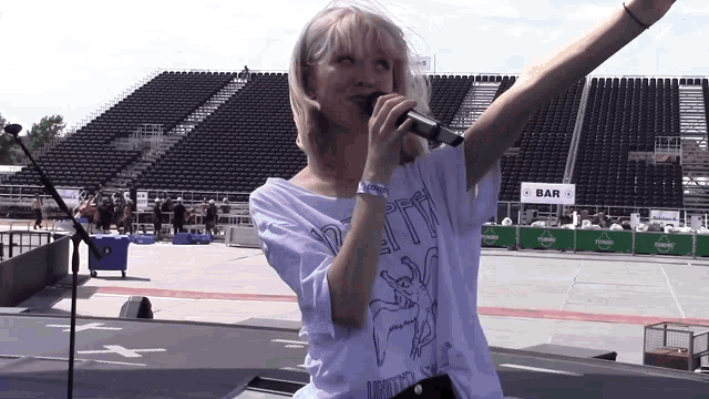 a woman is singing into a microphone in front of a bar sign