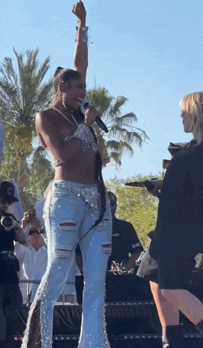 a woman singing into a microphone while wearing ripped jeans and a crop top