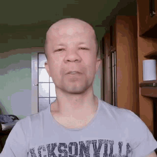 a bald man wearing a jacksonville t-shirt looks at the camera .