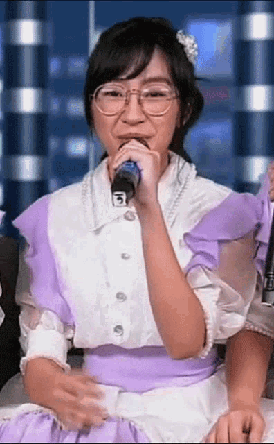 a girl with glasses is singing into a microphone with the letter b on it