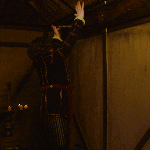 a woman in a black coat is reaching for something in a dark room with candles