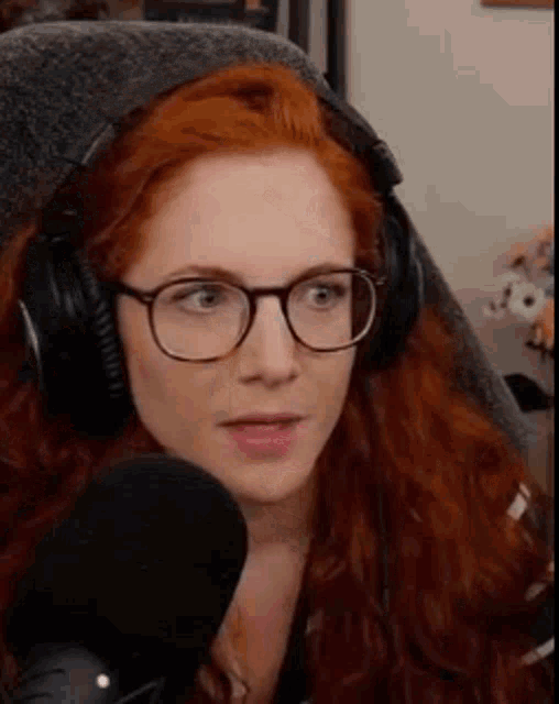 a woman with red hair and glasses is wearing headphones and talking into a microphone .