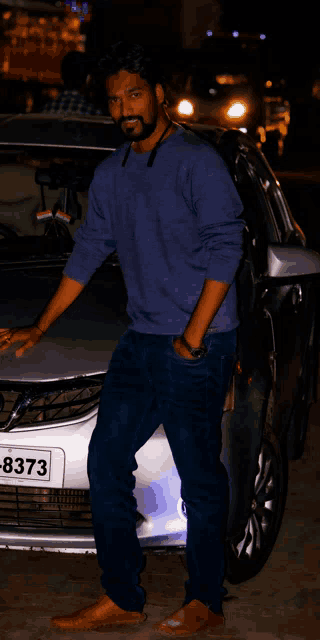 a man stands in front of a silver car with a license plate that says 8373