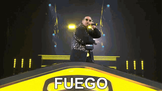 a man singing into a microphone on a stage with the word fuego on it