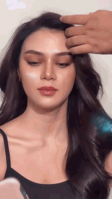 a woman in a black tank top is getting her hair styled