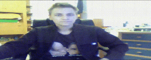 a man in a black jacket is sitting in a chair in front of a wall