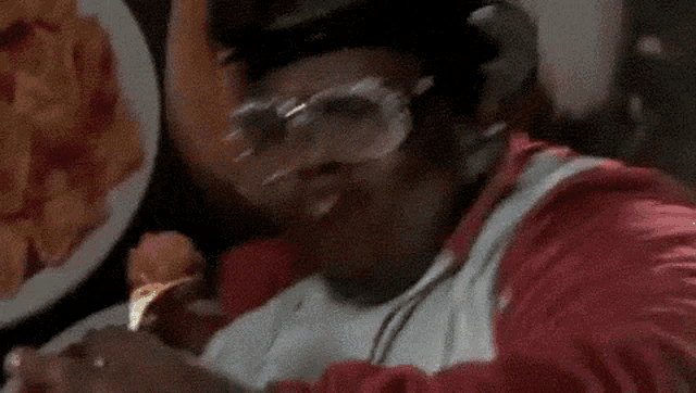 a man wearing glasses and a hat is eating a piece of food .