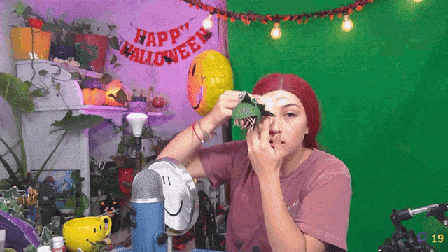 a woman is applying makeup in front of a green screen with a banner that says happy halloween
