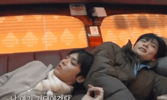 two men are sleeping in a car with a blanket on their heads .