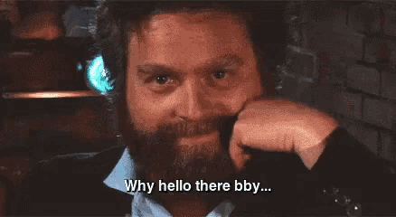 a man with a beard is talking on a cell phone and says " why hello there bby "