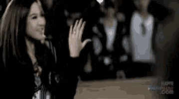 a woman is waving her hand in front of a crowd while talking on a cell phone .