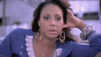 a woman in a blue shirt and earrings is holding her hand to her ear .