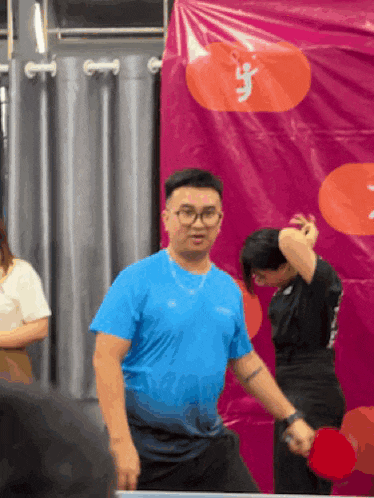 a man in a blue shirt is holding a ping pong paddle in front of a sign that says ' a '