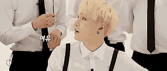 a man in a white shirt and suspenders is sitting in front of a group of men in suits .