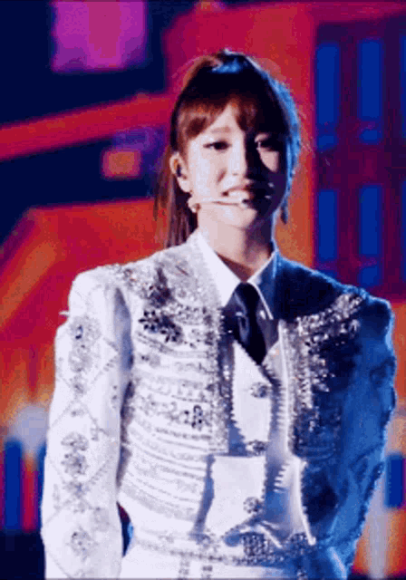 a woman in a white jacket and tie is standing in front of a microphone on a stage .